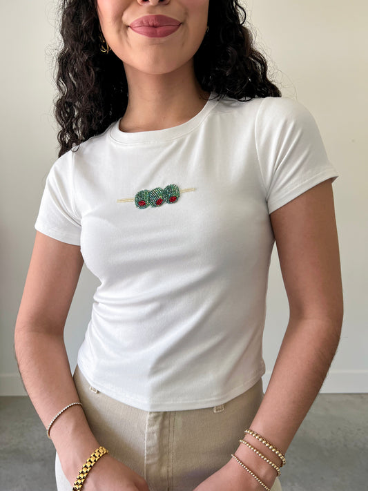 A woman wearing a white t-shirt with a beaded olive design on the front.